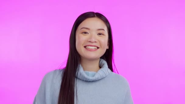 Woman, heart hand and portrait with a smile and love emoji sign in a studio. Asian female person, happy and valentines day icon gesture with pink background and hope for romance and kindness. - Footage, Video