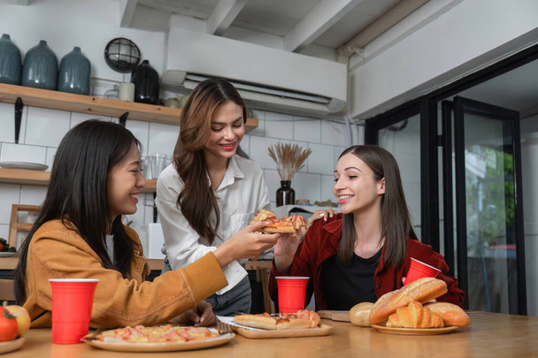 Un grupo de amigas jóvenes hacen una fiesta con pizza en la mesa y vasos rojos. Hablar y vivir juntos felices, divertirse en casa.. - Foto, Imagen