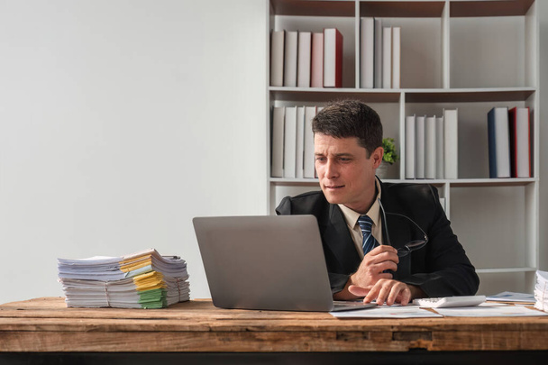 Unhappy young businessman feeling bored and stressed at work looking at laptop with hopeless expression while sitting in office. - Photo, Image