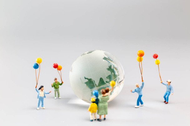 Miniaturowi ludzie, radosna rodzina z balonem otaczającym kryształową kulę ziemską i koncepcją Światowego Dnia Ziemi - Zdjęcie, obraz