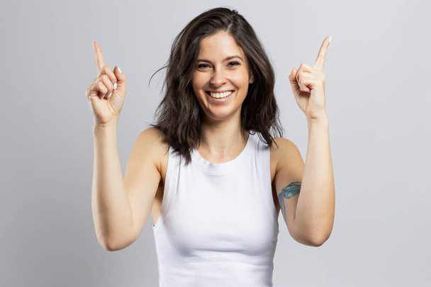 Beautiful happy brunette woman pointing away at some copy space, isolated on gray background - Photo, Image