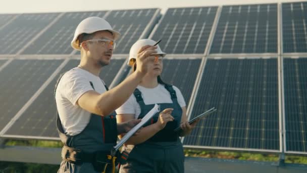 Una ingeniera y un trabajador en uniforme están revisando los paneles solares. Están trabajando en un proyecto de ahorro de energía. Los trabajadores están enfocados y discutiendo la efectividad del sistema.4K  - Metraje, vídeo