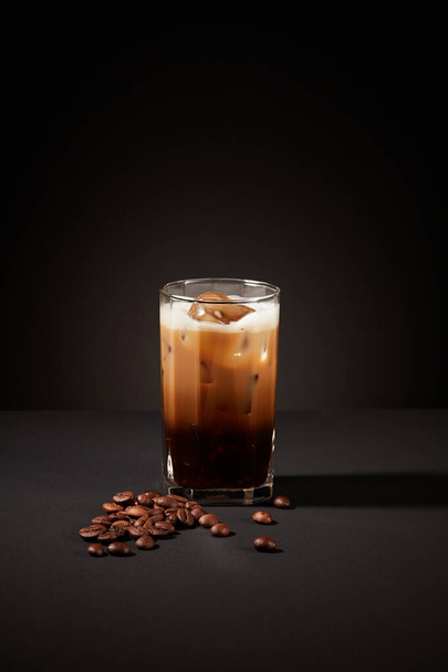 Крупный план чашки кофе с кофейными зернами на загадочном черном фоне. Кофе содержит витамины группы В и противовоспалительные средства, которые могут предотвратить прыщи, вызванные дерматитом. - Фото, изображение