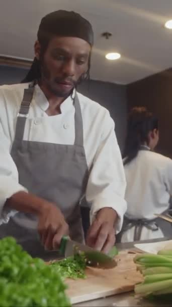 Pionowe ujęcie Afroamerykańskiego kucharza w fartuchu krojącego cebulę podczas przygotowywania sałatki dla gości w kuchni kawiarni - Materiał filmowy, wideo