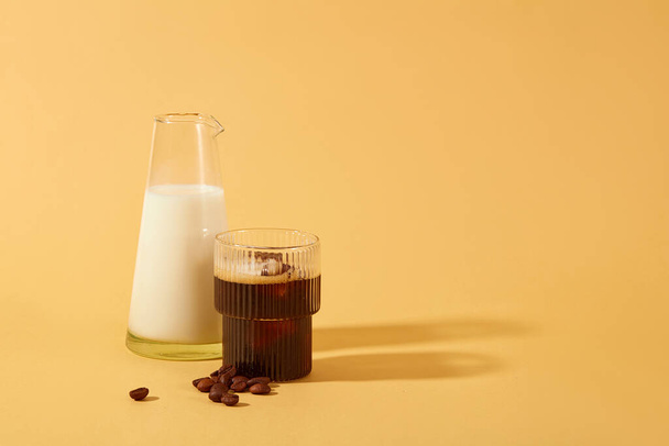 Een kop zwarte koffie, verse melk in een glazen pot en koffiebonen op een minimalistische achtergrond. Koffie is effectief in het overwinnen van huidschade veroorzaakt door UV-stralen en vrije radicalen. - Foto, afbeelding