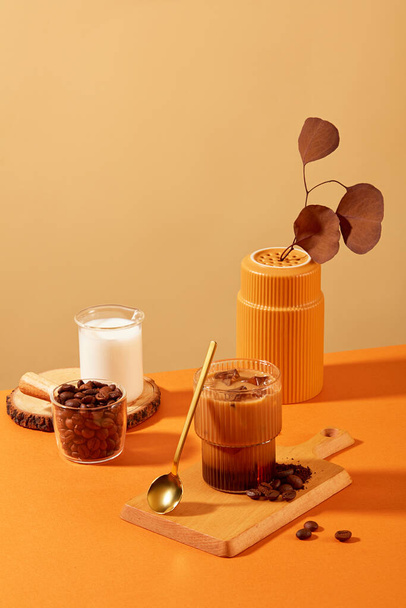 Xícara de café com leite e grãos de café em tábua de corte de madeira, cercada por adereços com fundo laranja-marrom. Grãos de café têm muitos benefícios para a saúde. - Foto, Imagem
