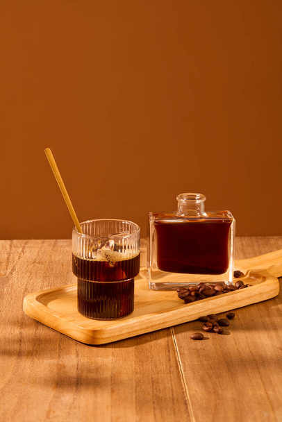 カップとコーヒーのボトルがコーヒー豆で木製のトレイに展示されています. 茶色の背景を持つ木製のテーブル. 広告のための絶妙な空間. - 写真・画像