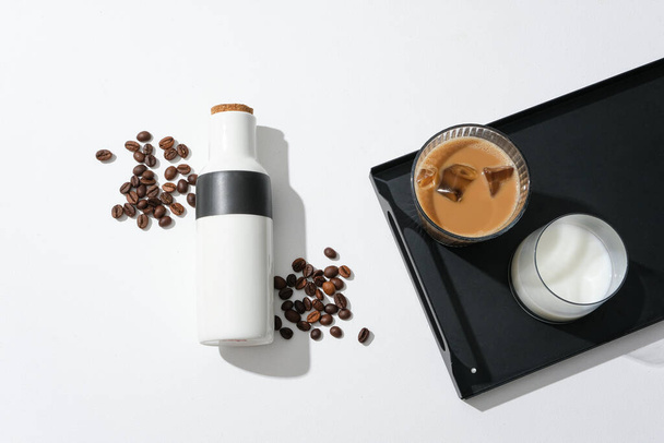 Op de zwarte schaal staat een kopje melk en een kopje melk koffie, een thermosfles en koffiebonen op een witte achtergrond. Cafeïne helpt het lichaam spierkracht te herstellen en de prestaties van de oefening te verbeteren. - Foto, afbeelding