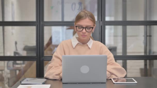 Mladá žena při pohledu na fotoaparát při práci na notebooku v kanceláři - Záběry, video