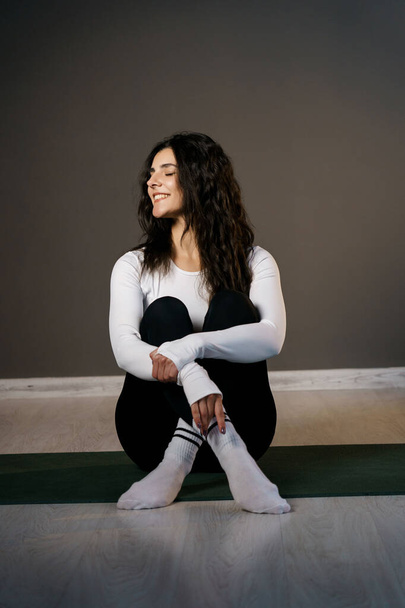 Красива жінка в білому спортивному одязі робить ранкові вправи на килимок і робить йогу - Фото, зображення