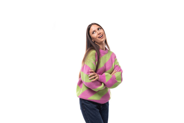melko positiivinen iloinen nuori eurooppalainen brunette nainen pukeutunut raidallinen vaaleanpunainen-vihreä villapaita valkoisella taustalla kopioi tilaa. - Valokuva, kuva