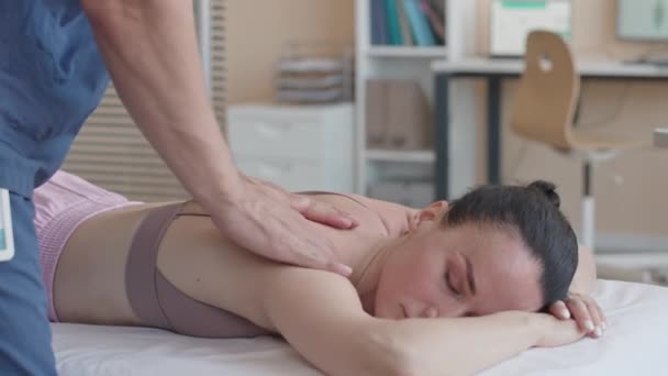 Fisioterapeuta masculino masajeando espalda de paciente mujer relajada acostada en sofá médico en clínica - Imágenes, Vídeo