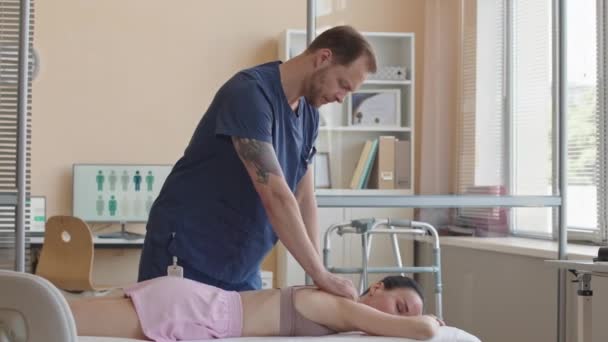 Femme couchée sur le canapé médical en tant que médecin masculin massant son dos pendant la séance de thérapie dans une clinique de bien-être - Séquence, vidéo
