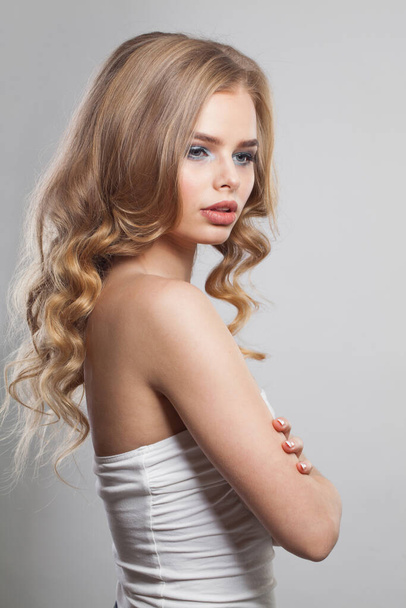 Belleza joven modelo femenino retrato. Mujer rubia con cabello largo y ondulado, maquillaje y piel limpia sobre fondo blanco - Foto, Imagen