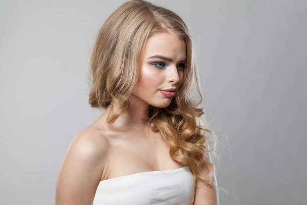Bonita modelo rubia joven con cabello largo y ondulado, maquillaje y piel limpia sobre fondo blanco. Retrato de mujer saludable - Foto, Imagen