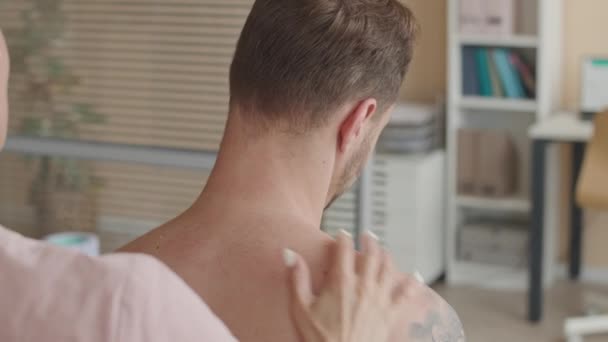 Sobre el hombro inyección de terapeuta de masaje femenino palpando los músculos de la espalda y el cuello de la paciente durante el examen médico en la clínica - Metraje, vídeo