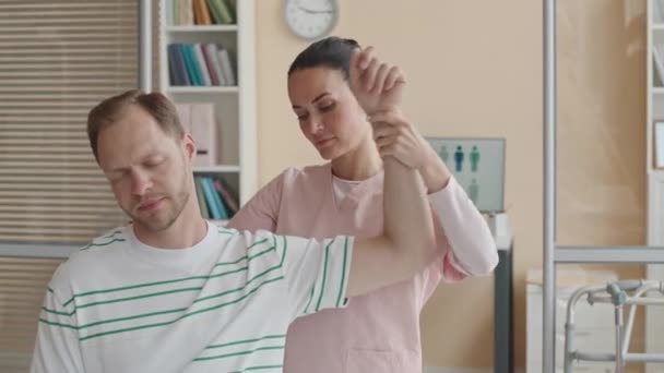 Fisioterapeuta feminina examinando ombro do homem durante consulta médica na clínica - Filmagem, Vídeo