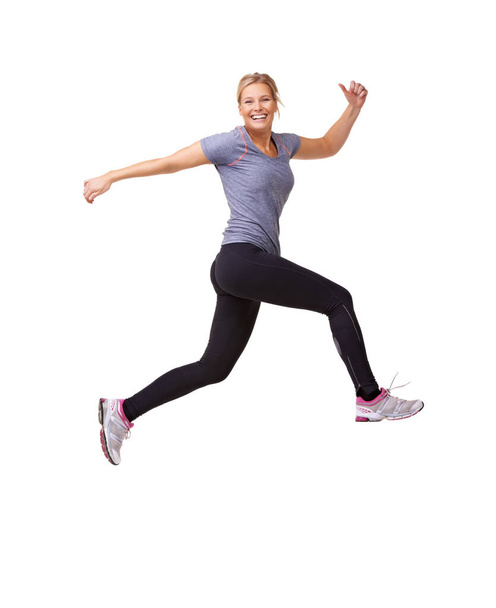 Woman, running and jump in studio for fitness, workout and training celebration, energy or achievement. Excited portrait of sports model or runner in air for exercise and cardio on a white background. - Photo, Image