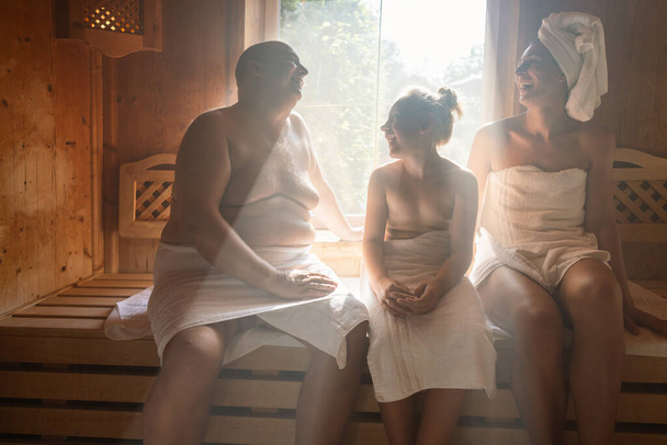 familia en una sauna finlandesa, hombre a la izquierda, mujer con toalla en la cabeza a la derecha, niño en el centro en el hotel spa - Foto, imagen