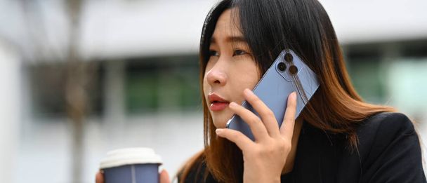 Horizontaal beeld van jonge zakenvrouw die op mobiele telefoon praat en wegkijkt. - Foto, afbeelding
