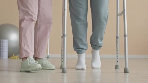 クリニックでのリハビリテーション治療中に女性の理学療法士をサポートして歩行フレームを使用して負傷した男性の足の低いセクションショット - 映像、動画