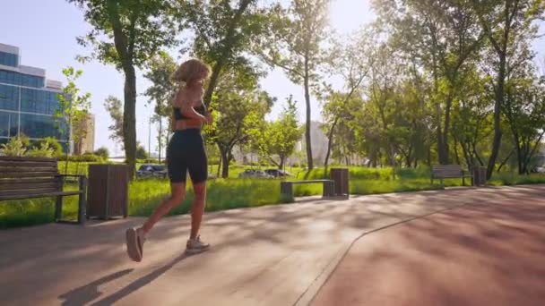vrouw joggen alleen in de ochtend stedelijke stad uitzicht zonnestralen door de boom takken fitness cardiotraining - Video