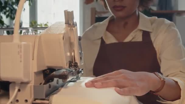 Obcięte ujęcie środkowe nierozpoznawalnego krawca wykonującego czarne szwy na białym kawałku tkanin przy użyciu maszyny odzieżowej w fabryce szycia - Materiał filmowy, wideo