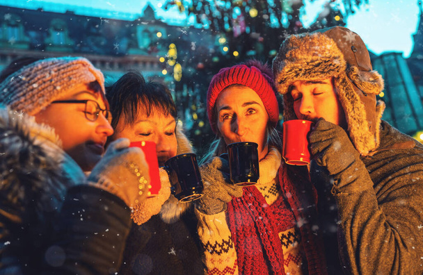 Счастливые друзья веселятся, выпивая глинтвейн и горячий шоколад на Рождество Марке - Фото, изображение