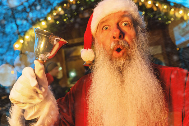 Weihnachtsmann mit überraschendem Blick, Glockengeläut auf dem Weihnachtsmarkt, festliche Lichterkulisse - Foto, Bild
