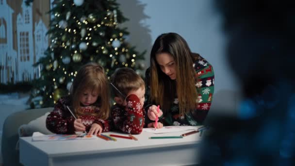 Lapset ja heidän äitinsä kirjoittavat kirjeen Joulupukille joulutunnelmassa. Hyvää lapsuuden lahjoja joulukuusi loma hymyilee ja toiveita lapsille. Laadukas 4k kuvamateriaalia - Materiaali, video