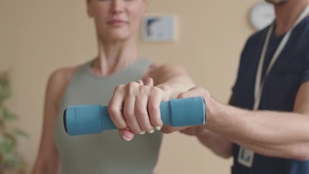 Vista da vicino di stringere la mano della donna che tiene i manubri con il supporto del fisioterapista maschile durante l'esercizio di riabilitazione in clinica - Filmati, video