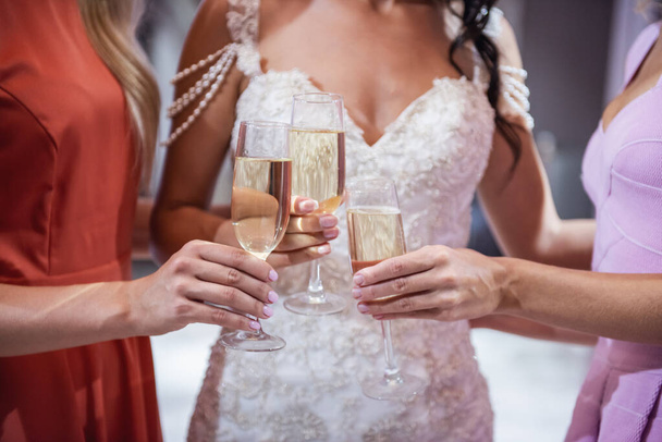 Hermosas mujeres jóvenes están bebiendo champán al elegir elegante vestido de novia en el salón de bodas moderno, recortado
 - Foto, imagen