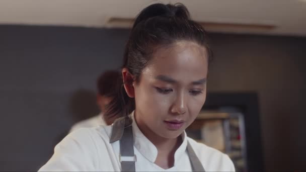 Tilt down shot of pensive female Asian cook finishing seafood pasta before serving to restaurant guests - Footage, Video