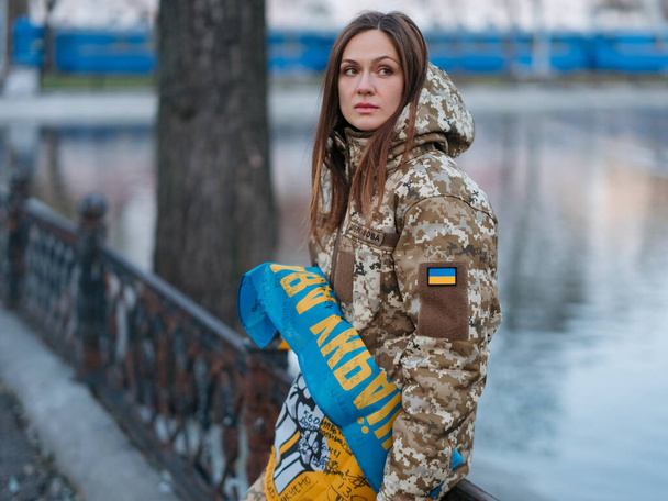 Ukraińska kobieta żołnierz posiadający flagę z podpisami ukraińskich wojowników i spoczywa w parku na wakacjach. Tłumaczenie z ukraińskiego: Siły Zbrojne Ukrainy, Chwała Ukrainie, nazwisko. - Zdjęcie, obraz