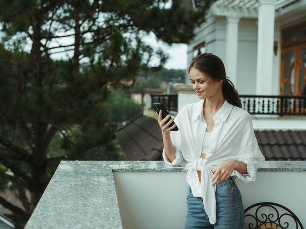 Mujer en el balcón de la casa con teléfono hermosa sonrisa en un día libre, hermosa vista de la naturaleza en las montañas, vacaciones de estilo de vida en el hotel. Foto de alta calidad - Foto, Imagen