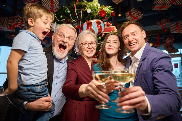 Niezwykle szczęśliwa radosna rodzina z kieliszkami szampana ciesząca się uroczystością Nowego Roku w kawiarni - Zdjęcie, obraz
