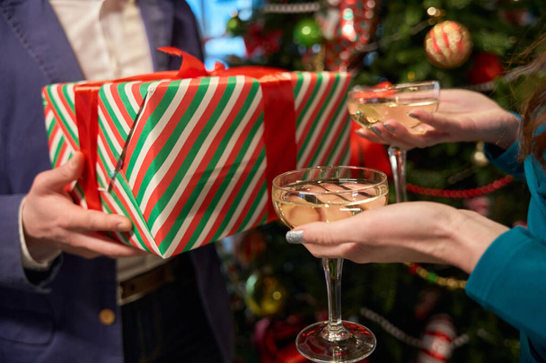 Donna irriconoscibile con bicchieri di champagne e uomo con scatola regalo durante la celebrazione di Capodanno nel ristorante - Foto, immagini
