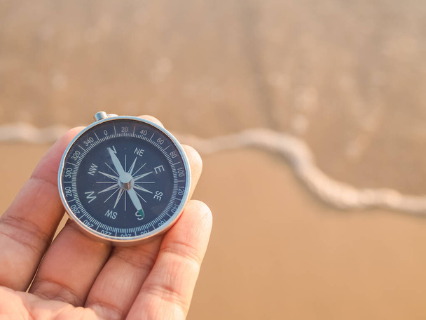 Закройте компас, держащий руку, на пляжном фоне - Фото, изображение