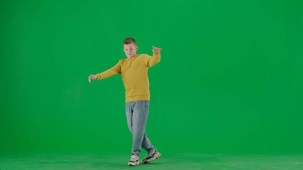 School kids and leisure time creative concept. Portrait of kid boy on chroma key green screen. Schoolboy in jeans dancing cool trend dance looking positive face expression. Full body front shot. - Foto, Imagen