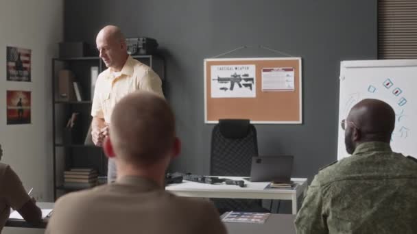 Panning tiro de caucasiano instrutor universitário careca leitura palestra sobre o uso de táticas militares durante a aula na academia militar - Filmagem, Vídeo