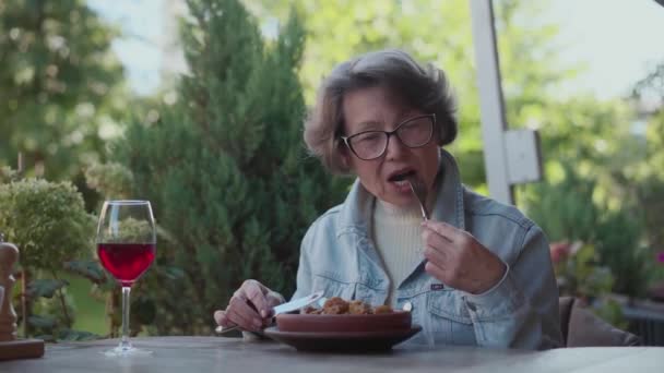 Eine ältere Frau kann sich das Frühstück in einem teuren Restaurant leisten. Rentnerin Touristin isst leckeres Mittagessen mit Rotwein im Terrassencafé. Denkende alte Reisende probieren Essen im Café. Hoch - Filmmaterial, Video