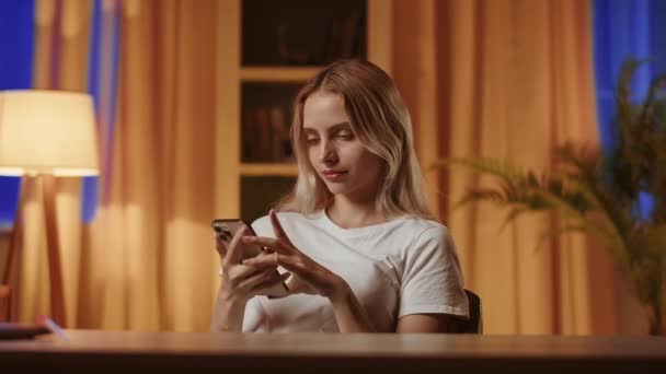A young blonde girl uses a smartphone, places bets in online casino. A smiling, satisfied lady in emotional upsurge experiences joy and jubilation from unexpected win and claps hands. The showcasing - Footage, Video