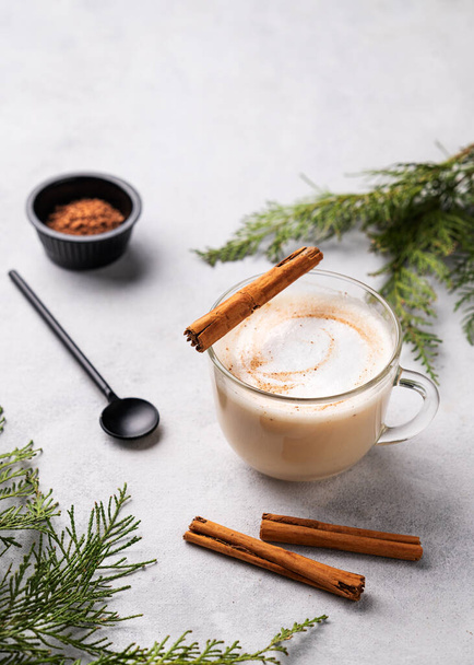 Gewürzkaffee Latte oder Cappuccino mit Zimtstangen auf hellem Hintergrund mit Tannenzweigen. Das Konzept eines weihnachtlichen Erwärmungsgetränks. Festliche Winterstimmung. Kopierraum. - Foto, Bild