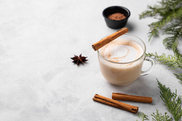 Gewürzkaffee Latte oder Cappuccino mit Zimtstangen und Anisstern auf hellem Hintergrund mit Tannenzweigen. Das Konzept eines weihnachtlichen Erwärmungsgetränks. Festliche Winterstimmung. Kopierraum. - Foto, Bild