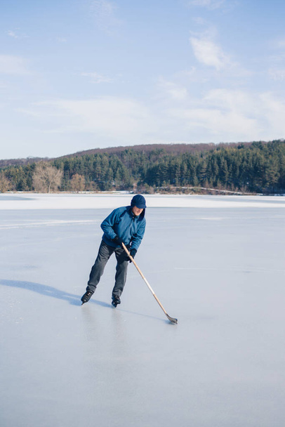 Starszy mężczyzna ćwiczy hokej na lodzie na zamarzniętym jeziorze w zimie. - Zdjęcie, obraz