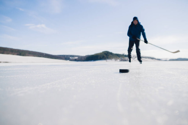 高齢者が冬の凍った湖にホッケースティックでパックをひねる練習. - 写真・画像