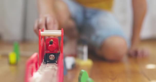 Un ragazzo sta giocando con una ferrovia per bambini. Il bambino gioca con i giocattoli di legno sul pavimento. Un trenino viaggia su una ferrovia di legno. Filmati 4k di alta qualità - Filmati, video