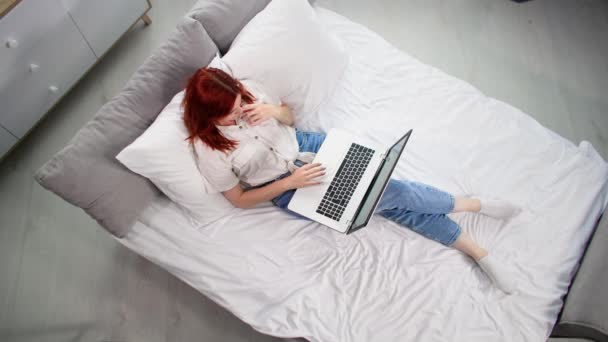 lavoro a casa, giovane donna che usa il computer portatile per guardare notizie su internet o per divertimento mentre si trova sul letto in camera, vista dall'alto - Filmati, video