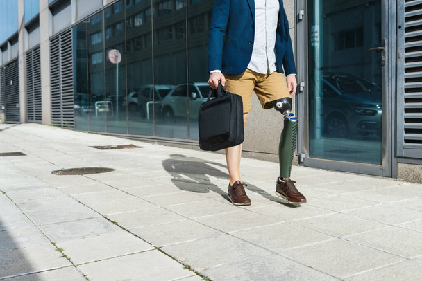 都市の設定で歩道を歩く人工足を持つ識別できない慎重な男性起業家. - 写真・画像