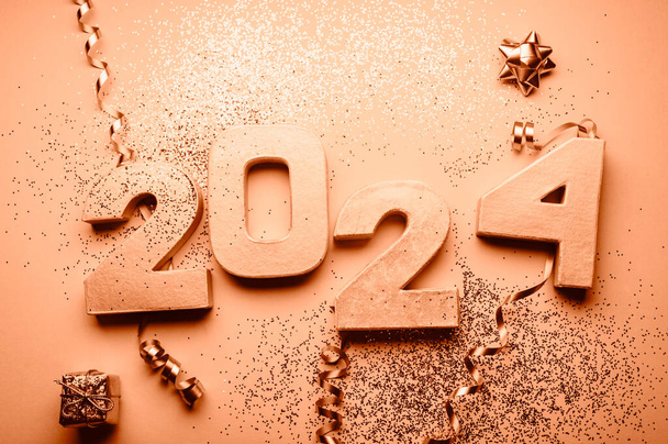 Goldene Ziffern 2024 mit Glitzer und Weihnachtsdekoration in der Nähe. Feiertagsdekoration oder Postkartenkonzept mit Draufsicht und Kopierraum. Toned in Peach Fuzz Farbe des Jahres 2024 - Foto, Bild